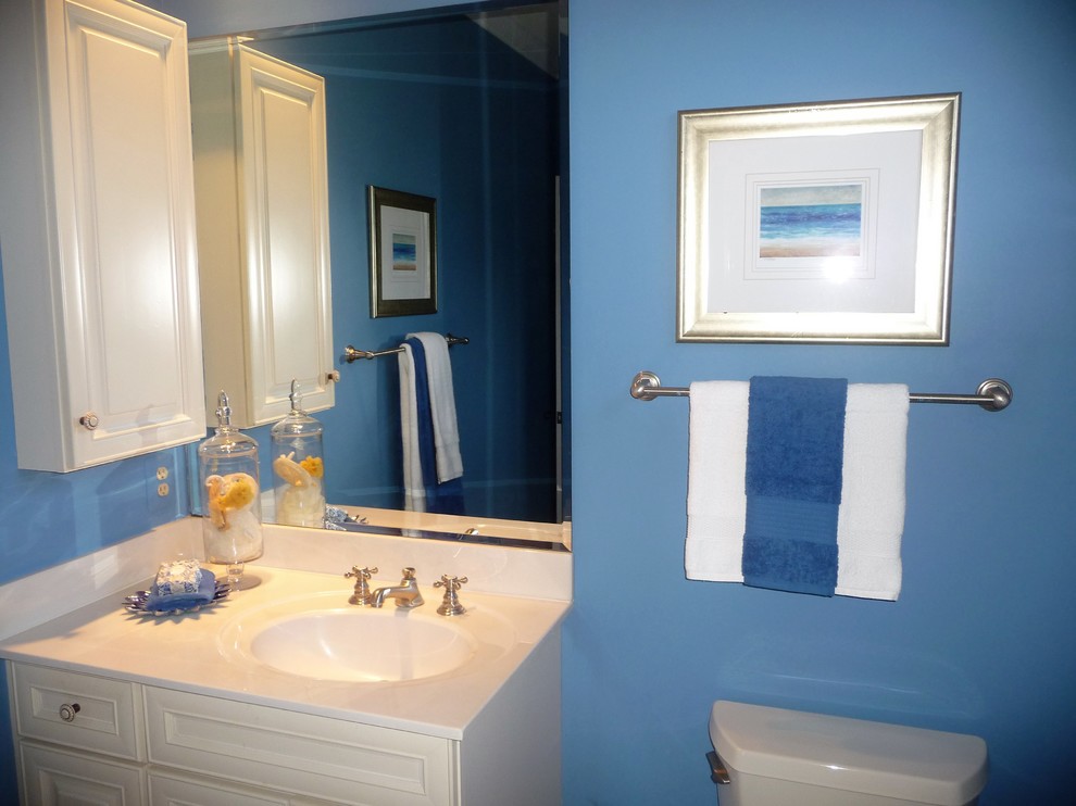 Modelo de cuarto de baño clásico de tamaño medio con armarios con paneles con relieve, puertas de armario blancas, sanitario de una pieza, paredes azules, aseo y ducha, lavabo integrado y encimera de laminado