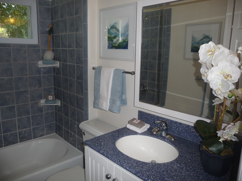 Réalisation d'une salle d'eau tradition de taille moyenne avec un placard à porte affleurante, des portes de placard blanches, une baignoire posée, un combiné douche/baignoire, WC à poser, un carrelage bleu, des carreaux de céramique, un mur blanc, une vasque et un plan de toilette en stratifié.