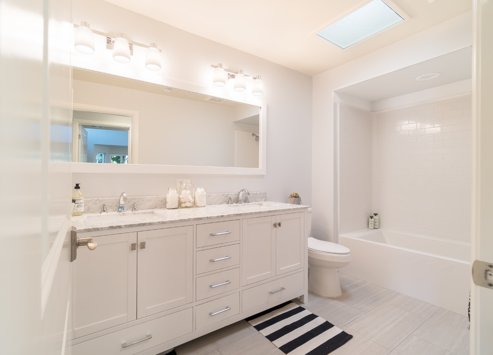 Imagen de cuarto de baño costero con armarios con paneles empotrados, puertas de armario blancas, bañera esquinera, paredes blancas, lavabo integrado y suelo gris