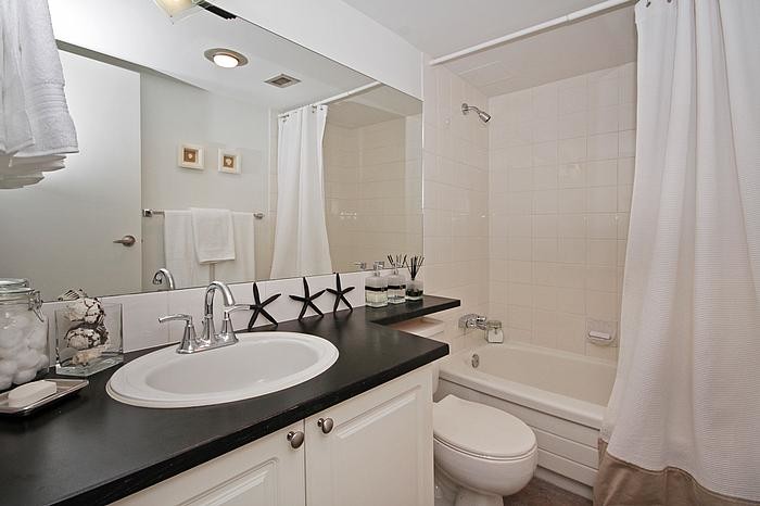Kleines Maritimes Badezimmer mit profilierten Schrankfronten, weißen Schränken, Duschbadewanne, Toilette mit Aufsatzspülkasten, weißen Fliesen, Keramikfliesen und weißer Wandfarbe in Sonstige