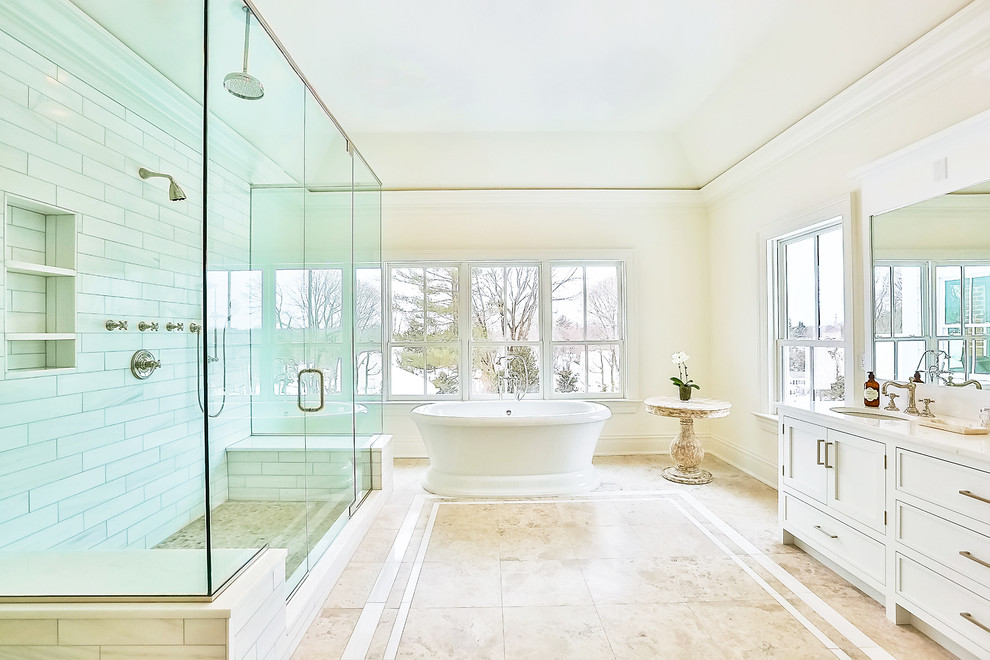 На фото: большая главная ванная комната в классическом стиле с белыми фасадами, отдельно стоящей ванной, душем в нише, белой плиткой, плиткой кабанчик, врезной раковиной, фасадами в стиле шейкер, бежевыми стенами, мраморным полом, столешницей из искусственного камня, бежевым полом и душем с распашными дверями с