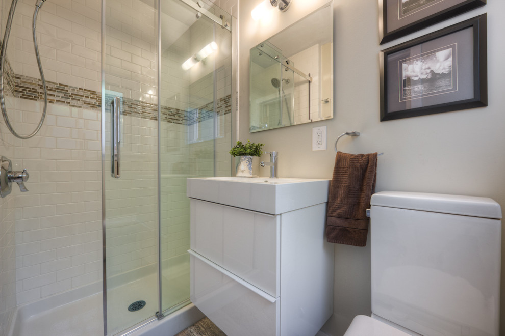 Kleines Klassisches Duschbad mit integriertem Waschbecken, flächenbündigen Schrankfronten, weißen Schränken, Mineralwerkstoff-Waschtisch, Duschnische, Wandtoilette mit Spülkasten, weißen Fliesen, Metrofliesen, beiger Wandfarbe und Schieferboden in Toronto