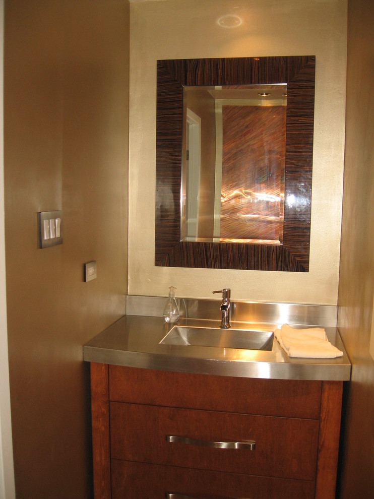 Modelo de cuarto de baño clásico renovado pequeño con armarios con paneles lisos, puertas de armario de madera oscura, paredes beige, aseo y ducha, lavabo integrado y encimera de acero inoxidable