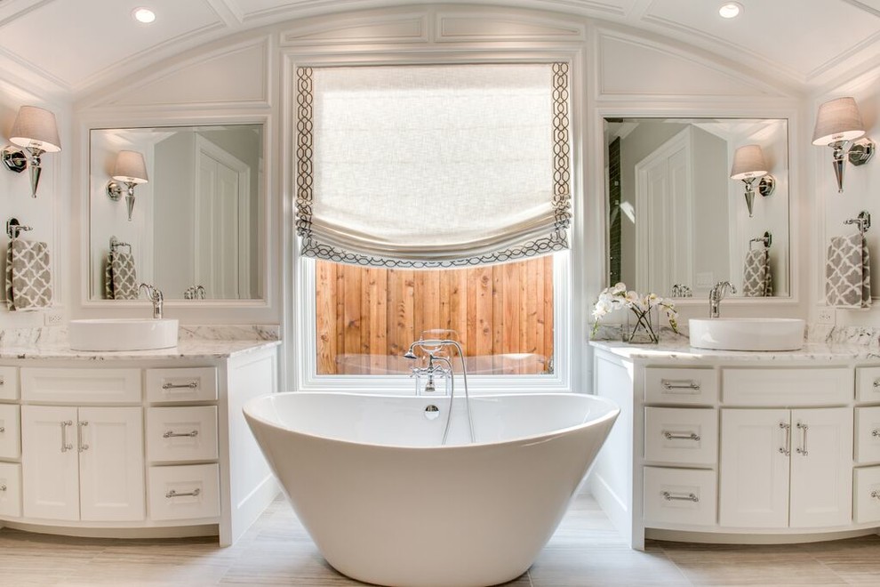 Modelo de cuarto de baño principal tradicional con puertas de armario blancas, bañera exenta, paredes blancas, lavabo sobreencimera y armarios con paneles empotrados