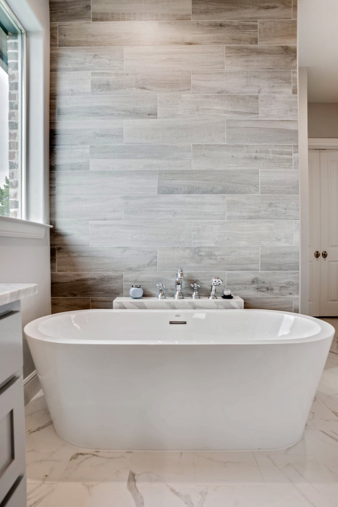 На фото: главная ванная комната в стиле неоклассика (современная классика) с отдельно стоящей ванной, серой плиткой, серыми стенами, полом из керамогранита и серым полом