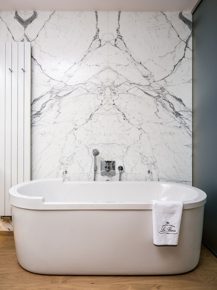 Immagine di una stanza da bagno padronale chic di medie dimensioni con vasca freestanding, piastrelle bianche, lastra di pietra, pareti grigie e parquet chiaro