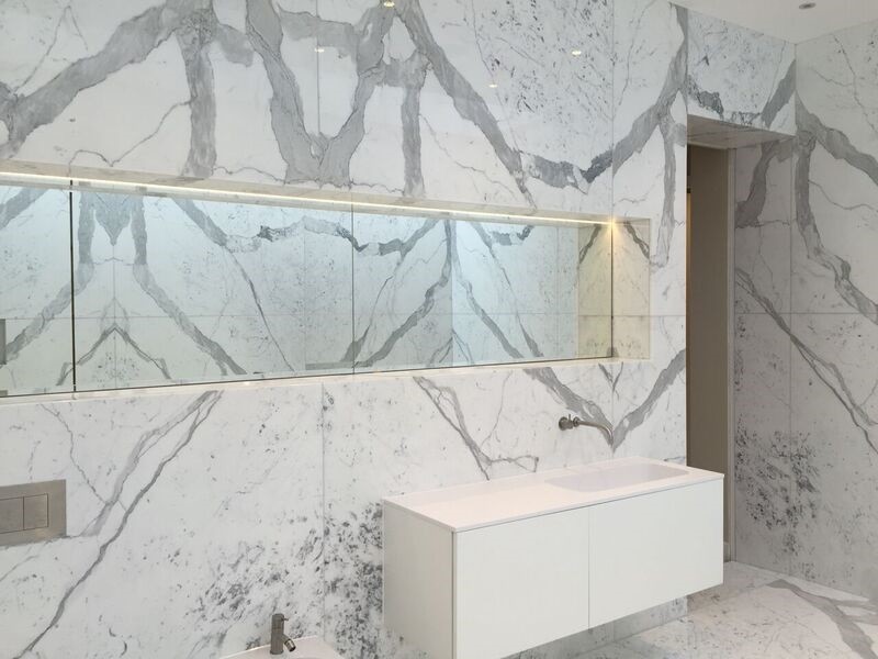 Cette image montre une grande salle de bain design avec un carrelage blanc, un carrelage de pierre, une baignoire indépendante, un mur blanc et un sol en marbre.