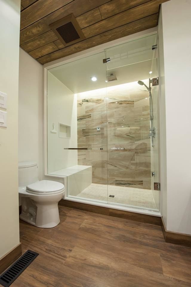 Cette photo montre une grande salle de bain principale tendance avec un placard à porte plane, des portes de placard blanches, une baignoire posée, une douche d'angle, WC à poser, un mur blanc, un sol en bois brun, un lavabo encastré et un plan de toilette en surface solide.