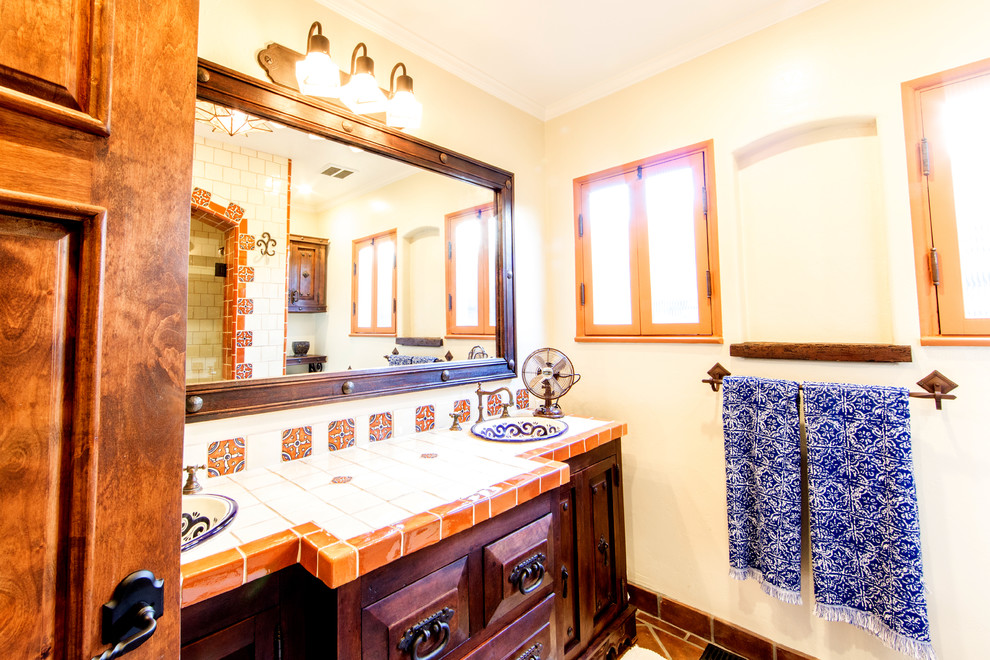 На фото: ванная комната среднего размера в средиземноморском стиле с фасадами с выступающей филенкой, коричневыми фасадами, ванной в нише, душем над ванной, оранжевой плиткой, керамической плиткой, белыми стенами, полом из терракотовой плитки, накладной раковиной, столешницей из плитки и душем с распашными дверями