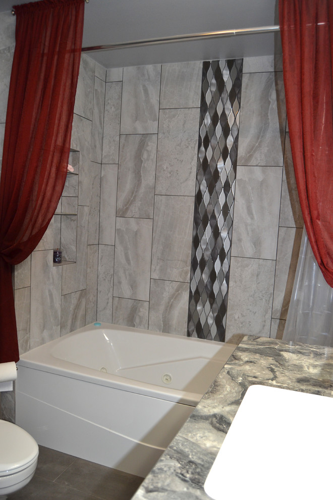 Inredning av ett klassiskt mellanstort grå grått en-suite badrum, med släta luckor, grå skåp, ett fristående badkar, en dusch/badkar-kombination, en toalettstol med separat cisternkåpa, grå kakel, porslinskakel, grå väggar, klinkergolv i porslin, ett undermonterad handfat, laminatbänkskiva, grått golv och dusch med duschdraperi