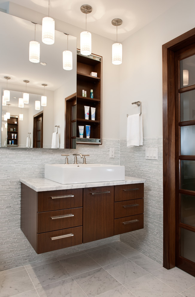 Cette image montre une salle de bain design en bois foncé avec une vasque, un placard à porte plane, un carrelage gris, des carreaux en allumettes et un mur blanc.
