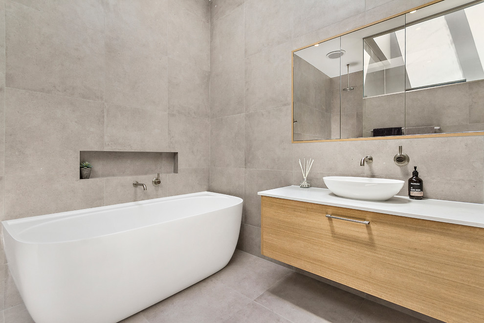Expansive contemporary ensuite wet room bathroom in Sydney with flat-panel cabinets, light wood cabinets, a freestanding bath, a one-piece toilet, grey tiles, ceramic tiles, grey walls, ceramic flooring, a vessel sink, engineered stone worktops, grey floors, an open shower and white worktops.