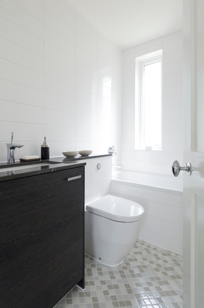 На фото: ванная комната в современном стиле с врезной раковиной, плоскими фасадами, темными деревянными фасадами, ванной в нише, унитазом-моноблоком, белой плиткой и серой столешницей с