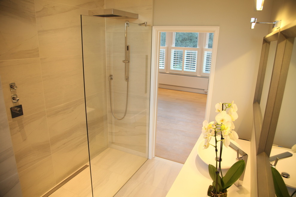 This is an example of a medium sized contemporary ensuite bathroom in London with flat-panel cabinets, light wood cabinets, a freestanding bath, a walk-in shower, a wall mounted toilet, beige tiles, stone slabs, beige walls, travertine flooring, a console sink, solid surface worktops, an open shower and white worktops.