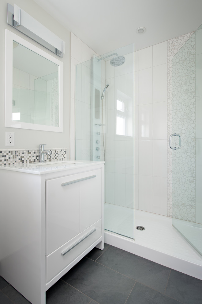 Klassisk inredning av ett litet badrum med dusch, med ett undermonterad handfat, släta luckor, vita skåp, marmorbänkskiva, en dusch i en alkov, en toalettstol med separat cisternkåpa, vit kakel, porslinskakel, grå väggar och klinkergolv i porslin