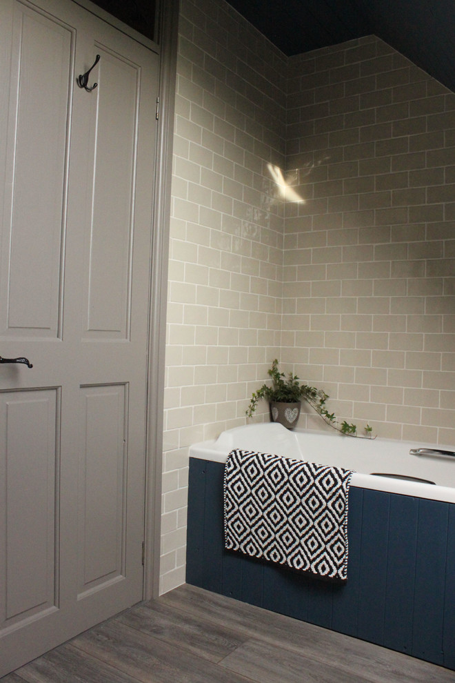 Bild på ett litet lantligt badrum för barn, med ett platsbyggt badkar, en toalettstol med separat cisternkåpa, beige kakel, keramikplattor, blå väggar, laminatgolv, ett piedestal handfat och grått golv