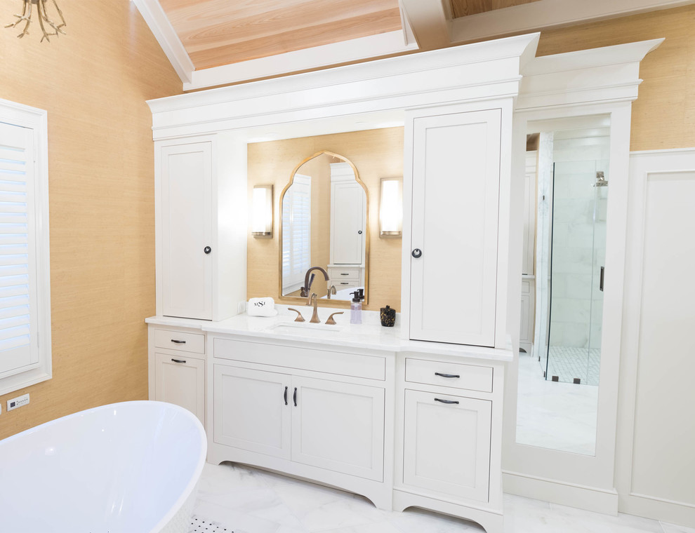 На фото: большая главная ванная комната в классическом стиле с фасадами с декоративным кантом, белыми фасадами, отдельно стоящей ванной, душем в нише, зеркальной плиткой, желтыми стенами, мраморным полом, врезной раковиной, столешницей из кварцита, белым полом и душем с распашными дверями
