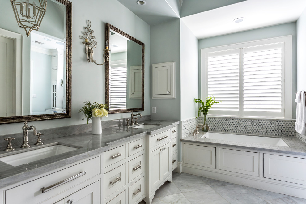 Idée de décoration pour une salle de bain principale tradition avec un placard à porte affleurante, des portes de placard blanches, une baignoire encastrée, carrelage en métal, un mur bleu, un lavabo encastré et un sol gris.