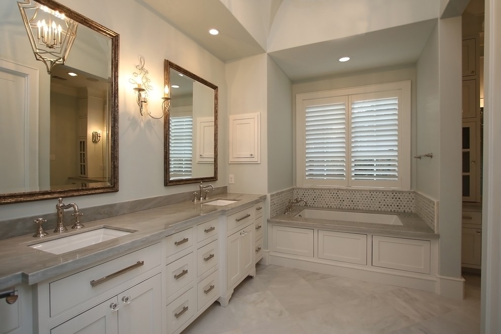 Esempio di una grande stanza da bagno padronale chic con ante a filo, pavimento in marmo, lavabo da incasso, top in pietra calcarea e vasca sottopiano
