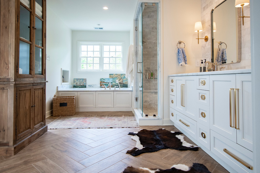 Свежая идея для дизайна: главная ванная комната среднего размера в стиле кантри с фасадами в стиле шейкер, белыми фасадами, полновстраиваемой ванной, белой плиткой, мраморной плиткой, белыми стенами, полом из керамогранита, мраморной столешницей, коричневым полом, душем с распашными дверями, белой столешницей и душем в нише - отличное фото интерьера