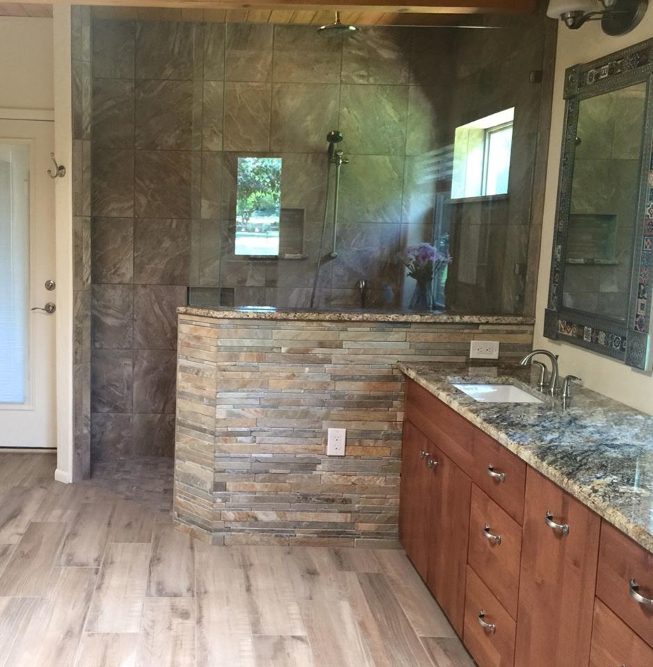 Photo of a medium sized rustic ensuite bathroom in Albuquerque with flat-panel cabinets, medium wood cabinets, a built-in bath, a walk-in shower, a one-piece toilet, beige tiles, white tiles, stone slabs, beige walls, light hardwood flooring, a built-in sink and solid surface worktops.