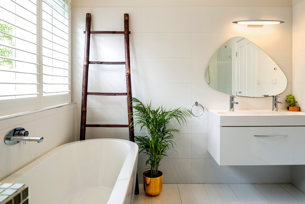 На фото: ванная комната в современном стиле с плоскими фасадами, белыми фасадами, отдельно стоящей ванной, керамической плиткой, белыми стенами, полом из керамической плитки, монолитной раковиной, серым полом, белой столешницей и белой плиткой