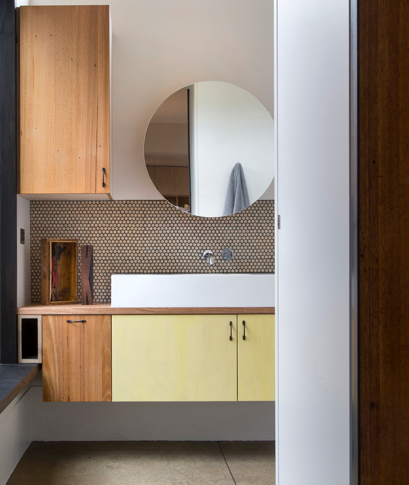 Cette image montre une salle de bain design avec un plan de toilette en bois, une vasque, un placard à porte plane, des portes de placard jaunes et un plan de toilette marron.