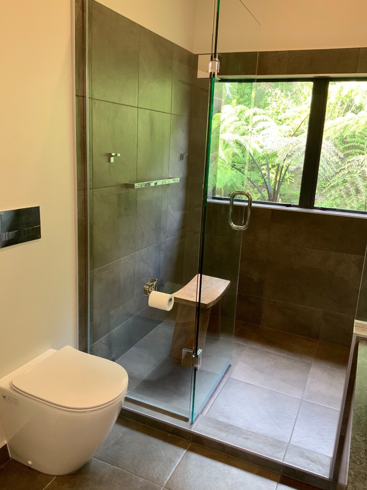 Large trendy gray tile and ceramic tile ceramic tile and gray floor double shower photo in Auckland with furniture-like cabinets, brown cabinets, a wall-mount toilet, gray walls, a vessel sink, granite countertops, a hinged shower door and black countertops