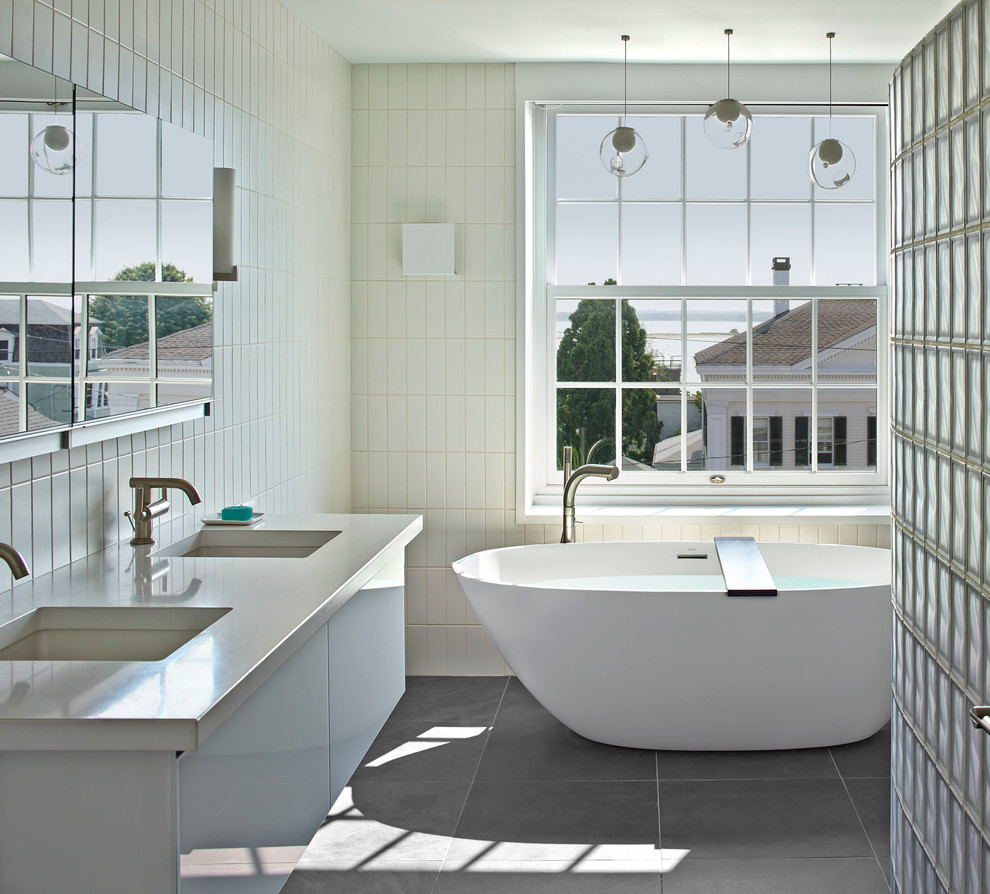 Idée de décoration pour une salle de bain principale design avec un lavabo encastré, un placard à porte plane, des portes de placard blanches, une baignoire indépendante, un carrelage blanc et une fenêtre.