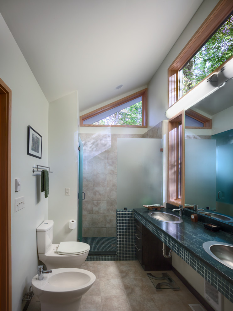 Modern inredning av ett litet en-suite badrum, med ett nedsänkt handfat, öppna hyllor, svarta skåp, granitbänkskiva, en dusch i en alkov, en toalettstol med separat cisternkåpa, svart kakel, mosaik, vita väggar och travertin golv