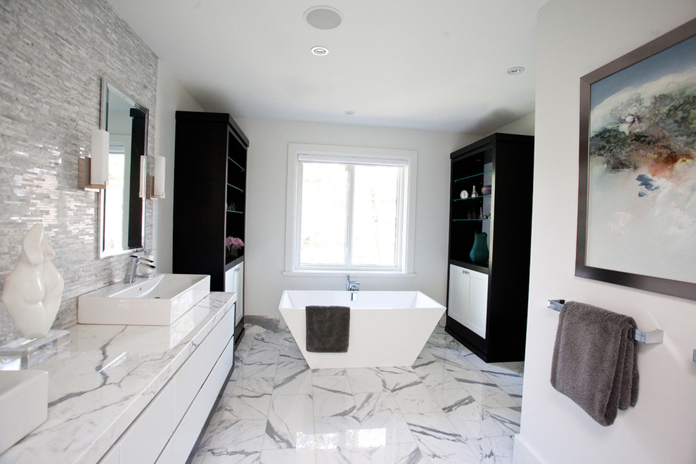 На фото: большая главная ванная комната в стиле модернизм с отдельно стоящей ванной, мраморной столешницей, настольной раковиной, плоскими фасадами, белыми фасадами, белой плиткой, каменной плиткой, серыми стенами и мраморным полом