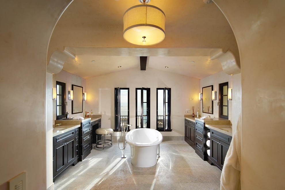 Example of a tuscan master beige tile and porcelain tile porcelain tile and beige floor freestanding bathtub design in Orange County with recessed-panel cabinets, dark wood cabinets, beige walls, an undermount sink and solid surface countertops