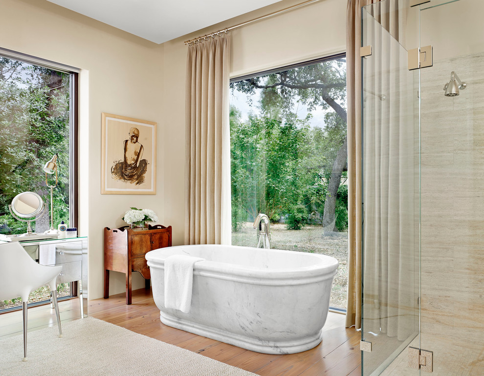 Aménagement d'une salle de bain méditerranéenne avec une baignoire indépendante, une douche d'angle, un carrelage beige, un mur beige et un sol en bois brun.