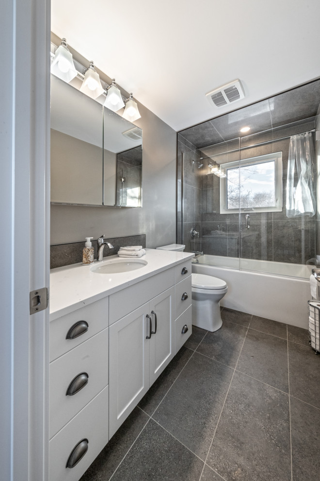 Cette photo montre une salle d'eau moderne de taille moyenne avec un placard à porte shaker, des portes de placard blanches, une baignoire en alcôve, un combiné douche/baignoire, WC à poser, un carrelage gris, des carreaux de céramique, un mur gris, un sol en carrelage de céramique, un lavabo encastré, un plan de toilette en granite, un sol gris, une cabine de douche à porte coulissante, un plan de toilette blanc, meuble simple vasque et meuble-lavabo encastré.