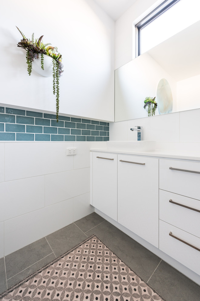 Inspiration for a medium sized contemporary family bathroom in Melbourne with flat-panel cabinets, white cabinets, a corner shower, a two-piece toilet, ceramic tiles, white walls, porcelain flooring, a vessel sink, engineered stone worktops, grey floors, a hinged door, white worktops, a freestanding bath and blue tiles.
