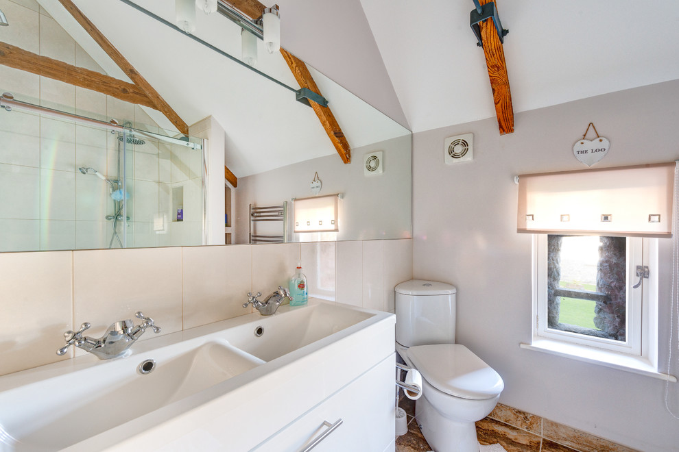На фото: ванная комната в стиле кантри с монолитной раковиной, белыми фасадами, душем в нише, раздельным унитазом и бежевой плиткой с