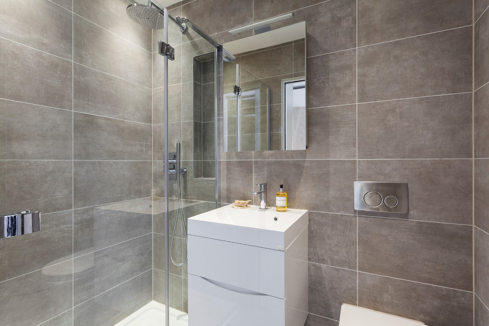Inspiration for a medium sized contemporary ensuite bathroom in London with white cabinets, a built-in shower, a wall mounted toilet, grey tiles, porcelain tiles, grey walls, porcelain flooring, a wall-mounted sink, grey floors and a hinged door.
