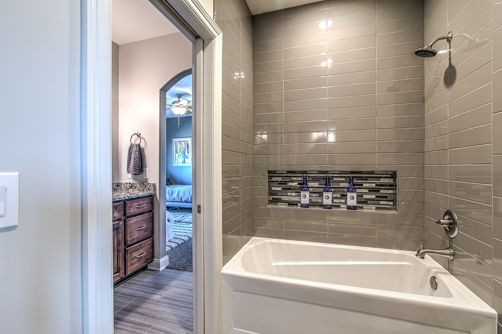 Photo of a medium sized classic bathroom in Omaha with raised-panel cabinets, medium wood cabinets, a built-in bath, a shower/bath combination, beige tiles, brown tiles, glass tiles, beige walls, light hardwood flooring, an integrated sink and granite worktops.