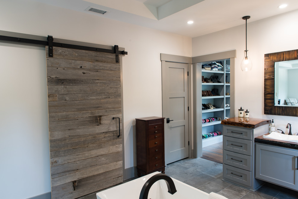 This is an example of a large rustic ensuite bathroom in Charleston with shaker cabinets, grey cabinets, a freestanding bath, a walk-in shower, beige walls, a built-in sink, wooden worktops, grey floors, an open shower and brown worktops.