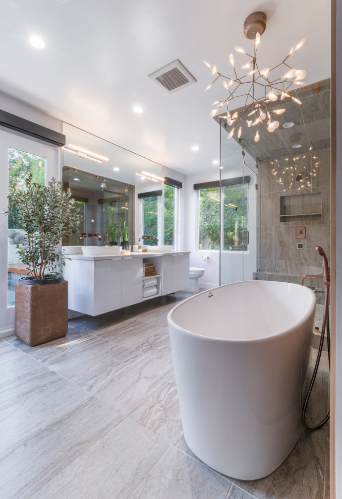 Inspiration for a large contemporary bathroom in Los Angeles with flat-panel cabinets, white cabinets, a freestanding bath, a one-piece toilet, brown tiles, porcelain tiles, white walls, porcelain flooring, a vessel sink, solid surface worktops, beige floors, a hinged door and white worktops.
