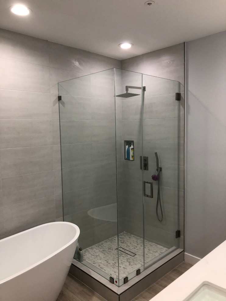 Cette image montre une grande salle de bain design avec une baignoire d'angle, un carrelage gris, des carreaux de béton, un mur gris, un sol en contreplaqué, un plan de toilette en surface solide, un sol beige, un plan de toilette blanc et une cabine de douche à porte battante.
