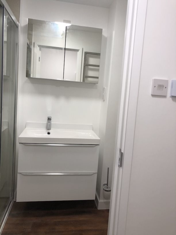 This is an example of a small modern shower room bathroom in Hampshire with louvered cabinets, white cabinets, white tiles, white walls, vinyl flooring, brown floors, white worktops, a single sink and a floating vanity unit.