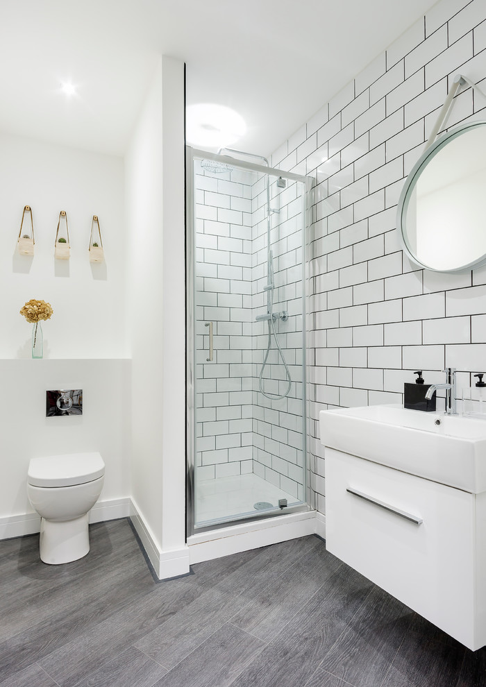 Exempel på ett skandinaviskt badrum, med släta luckor, vita skåp, en hörndusch, en toalettstol med hel cisternkåpa, vit kakel, tunnelbanekakel, vita väggar, mörkt trägolv, ett väggmonterat handfat och grått golv