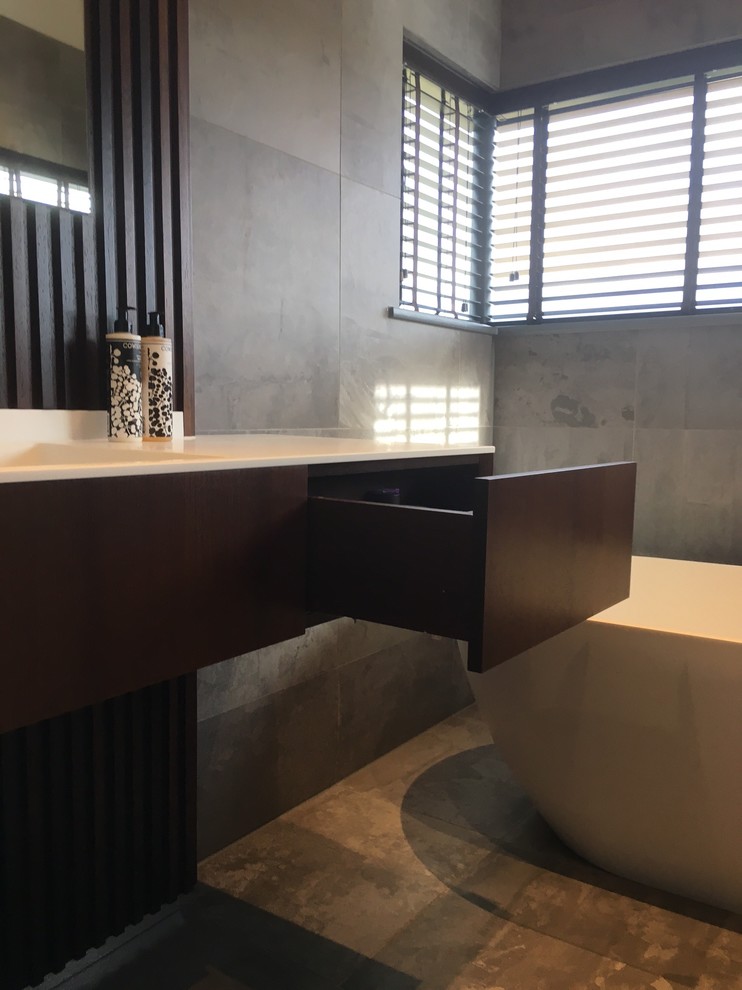 Exemple d'une petite salle de bain principale tendance en bois foncé avec un placard à porte affleurante, une baignoire indépendante, WC suspendus, un carrelage gris, des carreaux de céramique, un mur gris, un sol en carrelage de céramique, un lavabo intégré et un plan de toilette en quartz modifié.