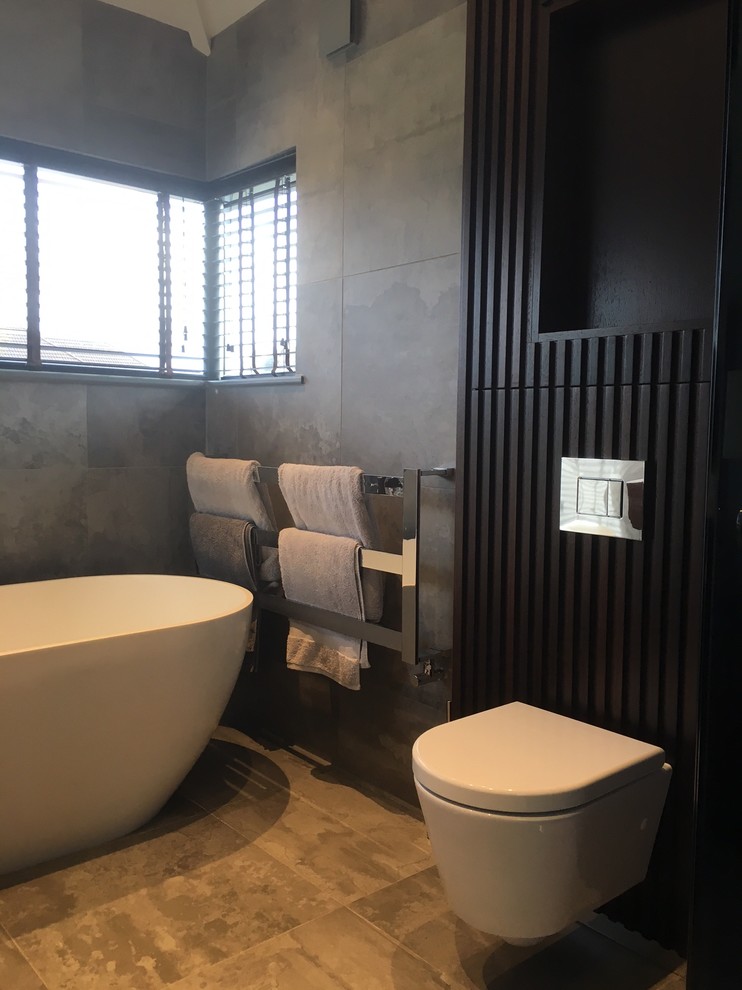 Small contemporary ensuite bathroom in Other with beaded cabinets, dark wood cabinets, a freestanding bath, a wall mounted toilet, grey tiles, ceramic tiles, grey walls, ceramic flooring, an integrated sink and engineered stone worktops.