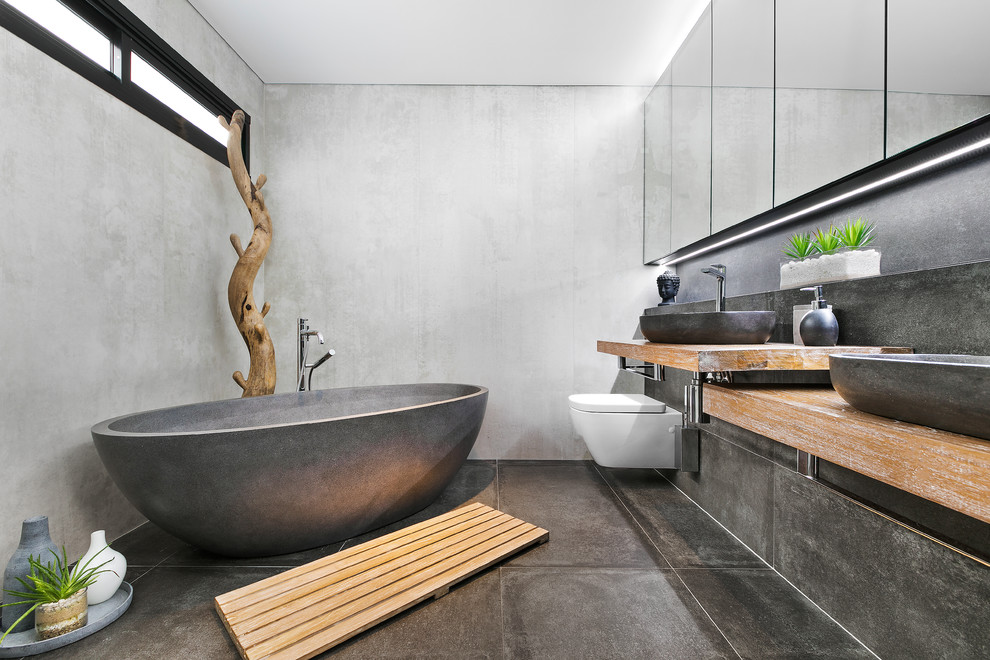 Пример оригинального дизайна: главная ванная комната в современном стиле с отдельно стоящей ванной, серыми стенами, настольной раковиной, серым полом, столешницей из дерева и коричневой столешницей
