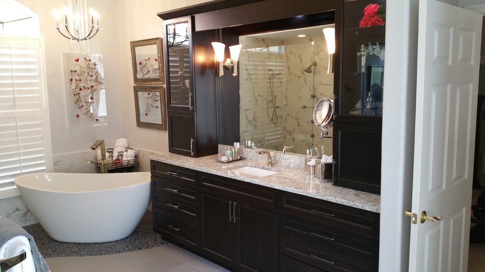 Design ideas for a large traditional ensuite bathroom in Tampa with a submerged sink, recessed-panel cabinets, dark wood cabinets, engineered stone worktops, a freestanding bath, a built-in shower, a one-piece toilet, grey tiles, porcelain tiles, white walls and pebble tile flooring.