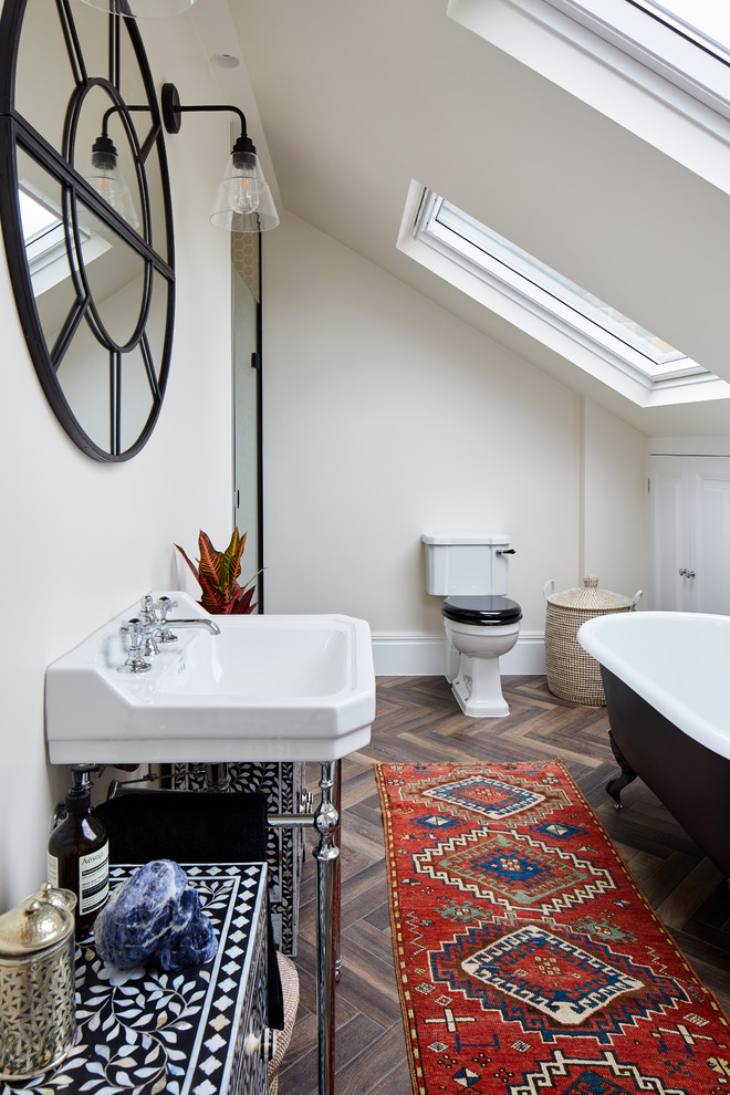 Photo of a bohemian bathroom in London with a claw-foot bath, a two-piece toilet, beige walls, dark hardwood flooring, a console sink and brown floors.
