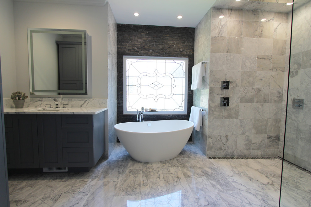 Cette photo montre une grande salle de bain principale tendance avec un placard à porte shaker, des portes de placard grises, une baignoire indépendante, une douche à l'italienne, WC séparés, un carrelage noir et blanc, un carrelage gris, un carrelage blanc, un carrelage de pierre, un mur gris, un sol en marbre, un lavabo encastré et un plan de toilette en marbre.