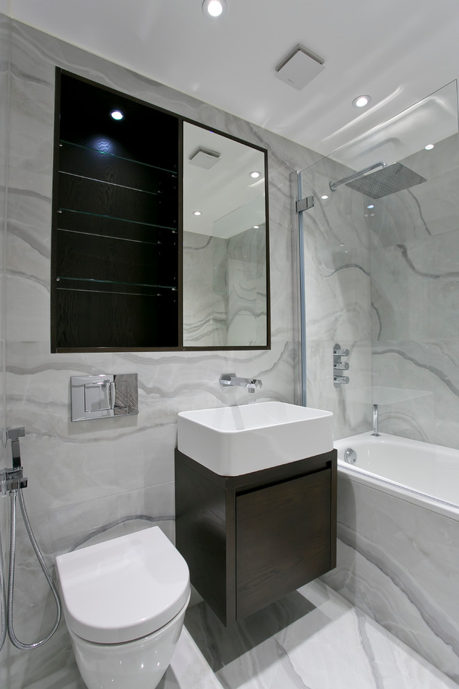 Modernes Badezimmer mit Aufsatzwaschbecken, flächenbündigen Schrankfronten, dunklen Holzschränken, Badewanne in Nische, Duschbadewanne, Wandtoilette und grauen Fliesen in London
